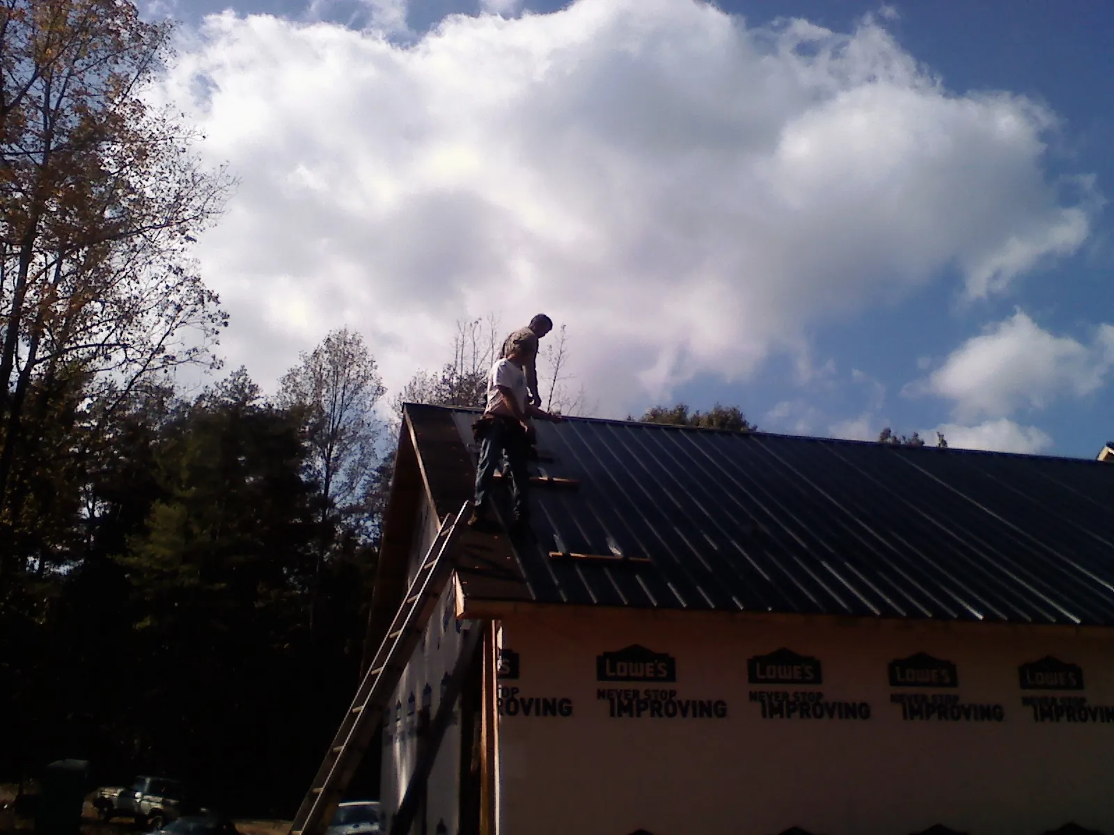 Roofer fastening dark metal panels high against a cloudy sky, from a Roof Inspection job in Kathleen