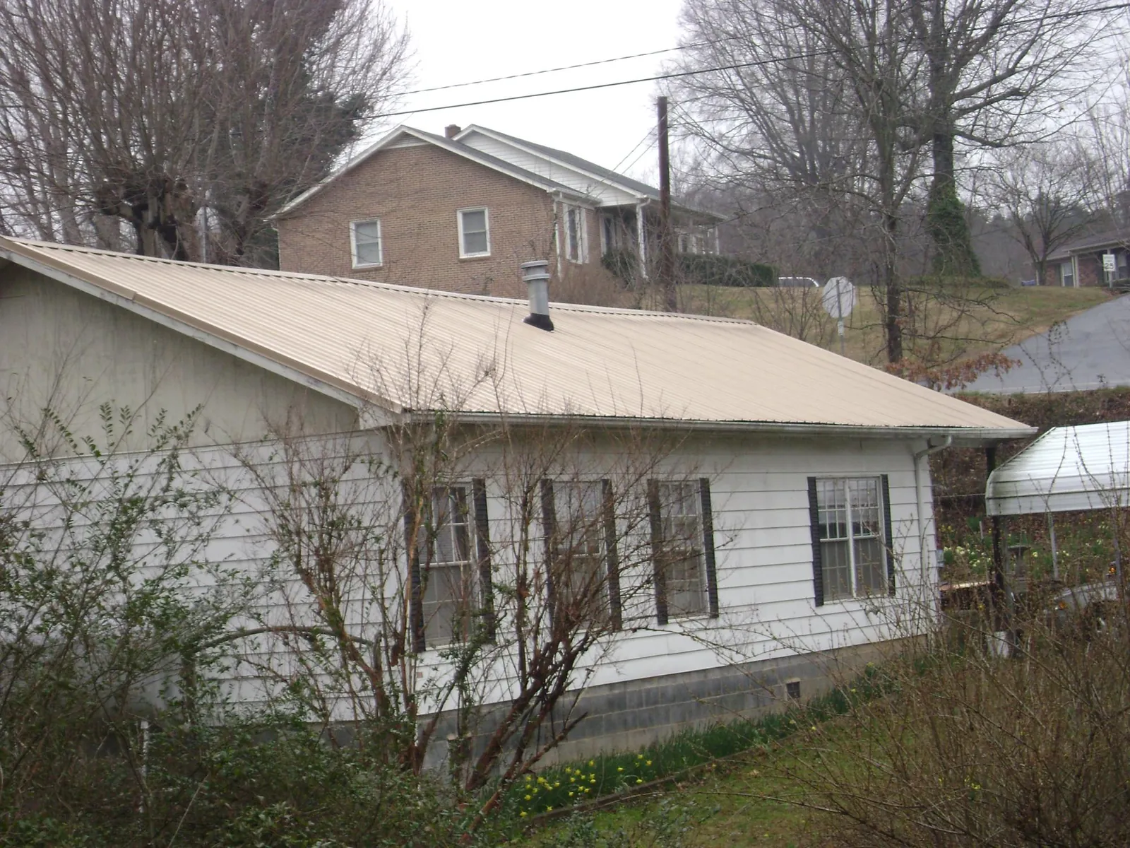 Tan metal roof on a white sided house set into a hillside — Commercial Roofing by Roofing Brothers in Kathleen