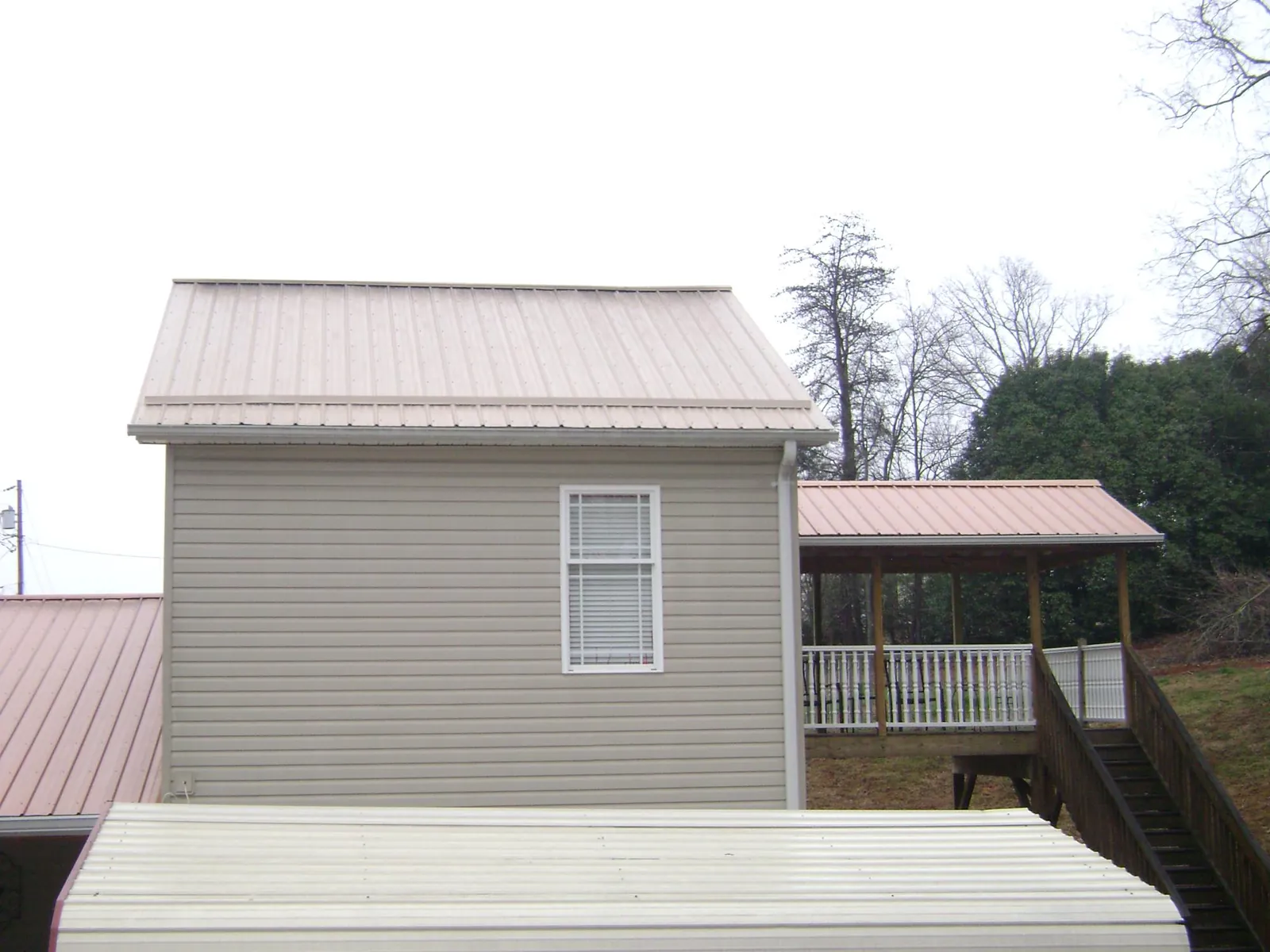 Tan metal roofs on a two story addition and attached porch, from a Roof Replacement job in Kathleen
